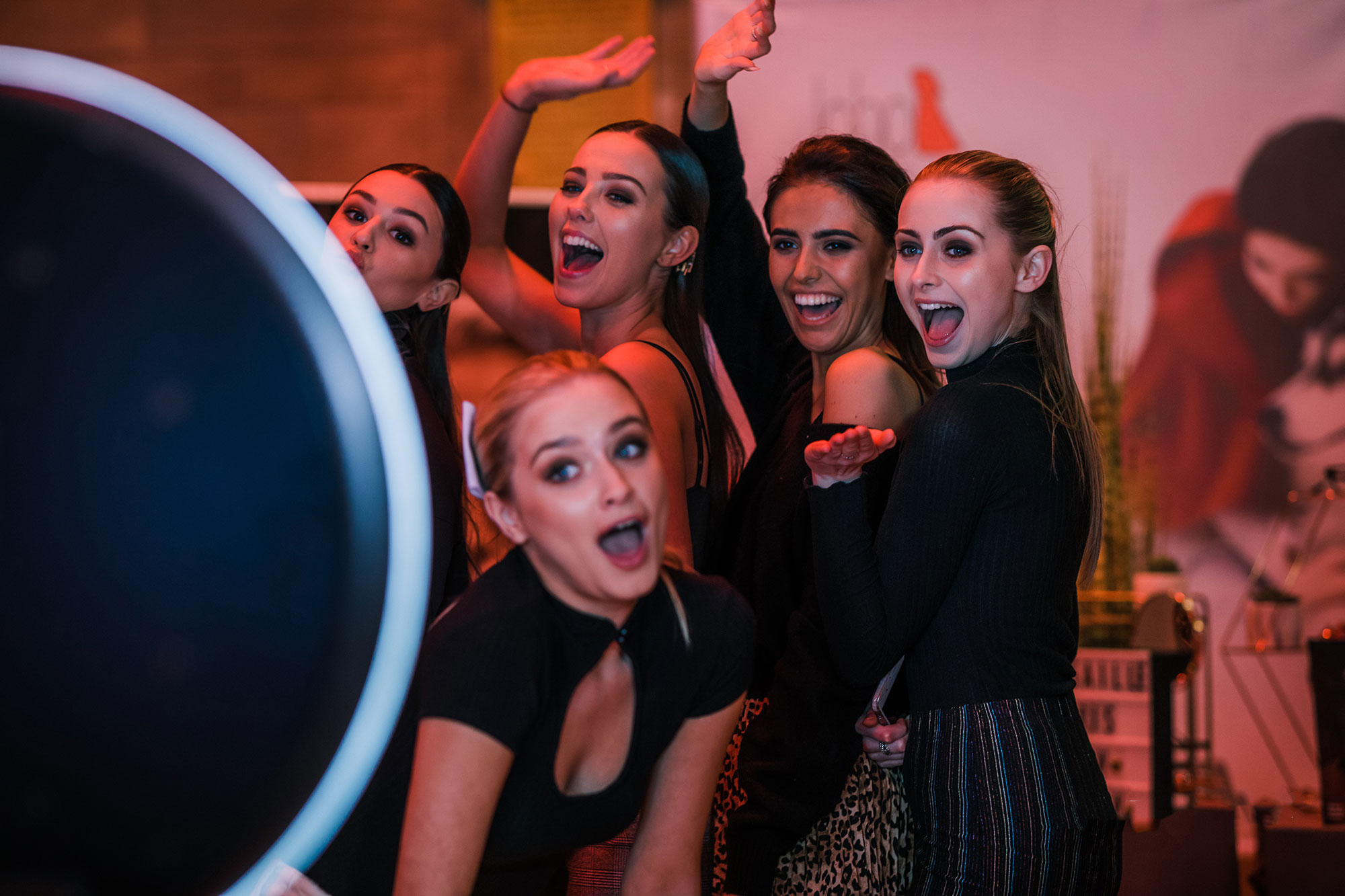 Fem glada kvinnor poserar framför en Magic Mirror fotobås, leende och gestikulerande, vilket skapar en